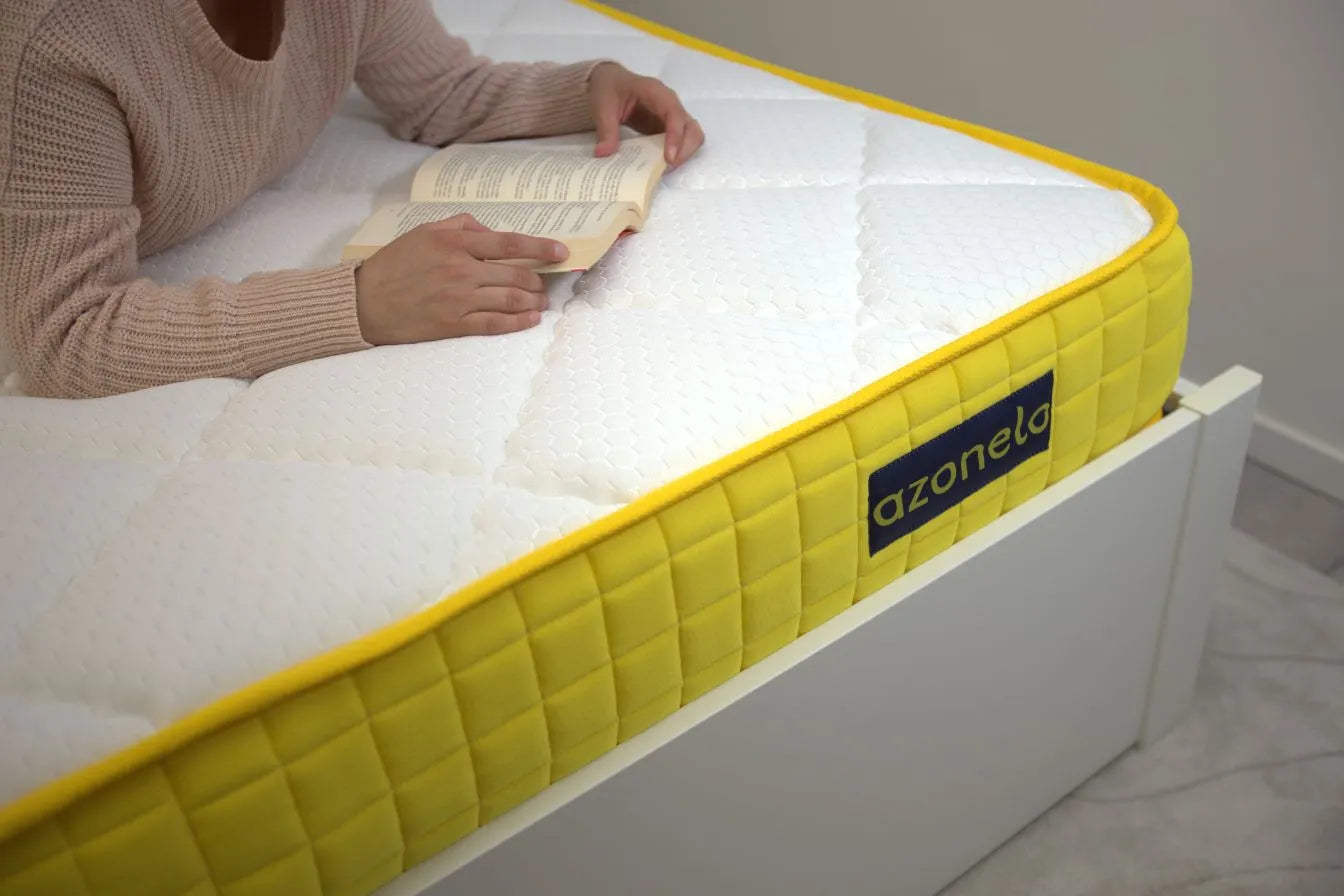 Osoba pohodlne relaxuje s knihou na 21 cm vysokom matraci Azonelo Yellow, ktorý má prešívaný biely poťah a výrazný žltý bok