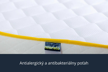 Detailný záber na čistý biely poťah s moderným žltým lemovaním a látkovou nášivkou s logom Azonelo. Materiál je mäkký na dotyk, priedušný a upravený tak, aby bol vhodný pre alergikov.
