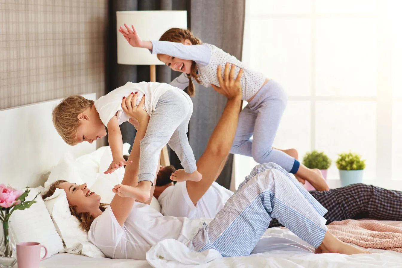 Šťastná rodina sa hrá ráno v posteli plná energie, vďaka prebudeniu bez bolesti na ortopedickom matraci Azonelo Yellow s pamäťovou penou.