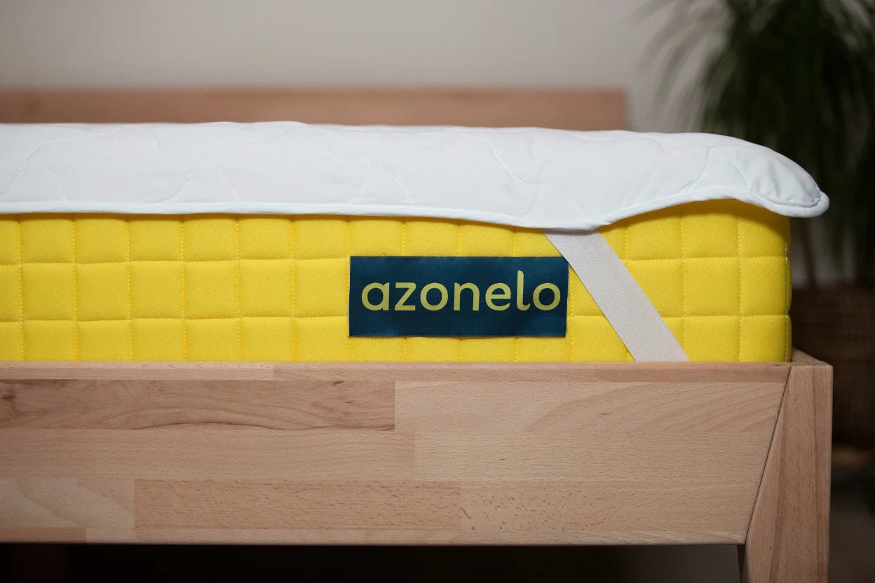 Žltý slovenský matrac Azonelo umiestnený na drevenej posteli, detail na uchytenie matracového chrániča.