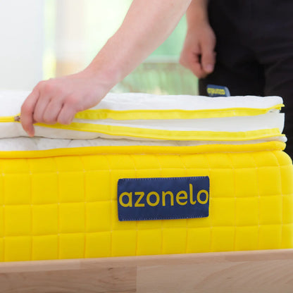 Osoba rozopína žltý zips na slovenskom ručne šitom vrchnom matraci Azonelo Dream, ktorý spája 4 cm pamäťovej peny a praktický poťah zo 100 percentného polyesteru.